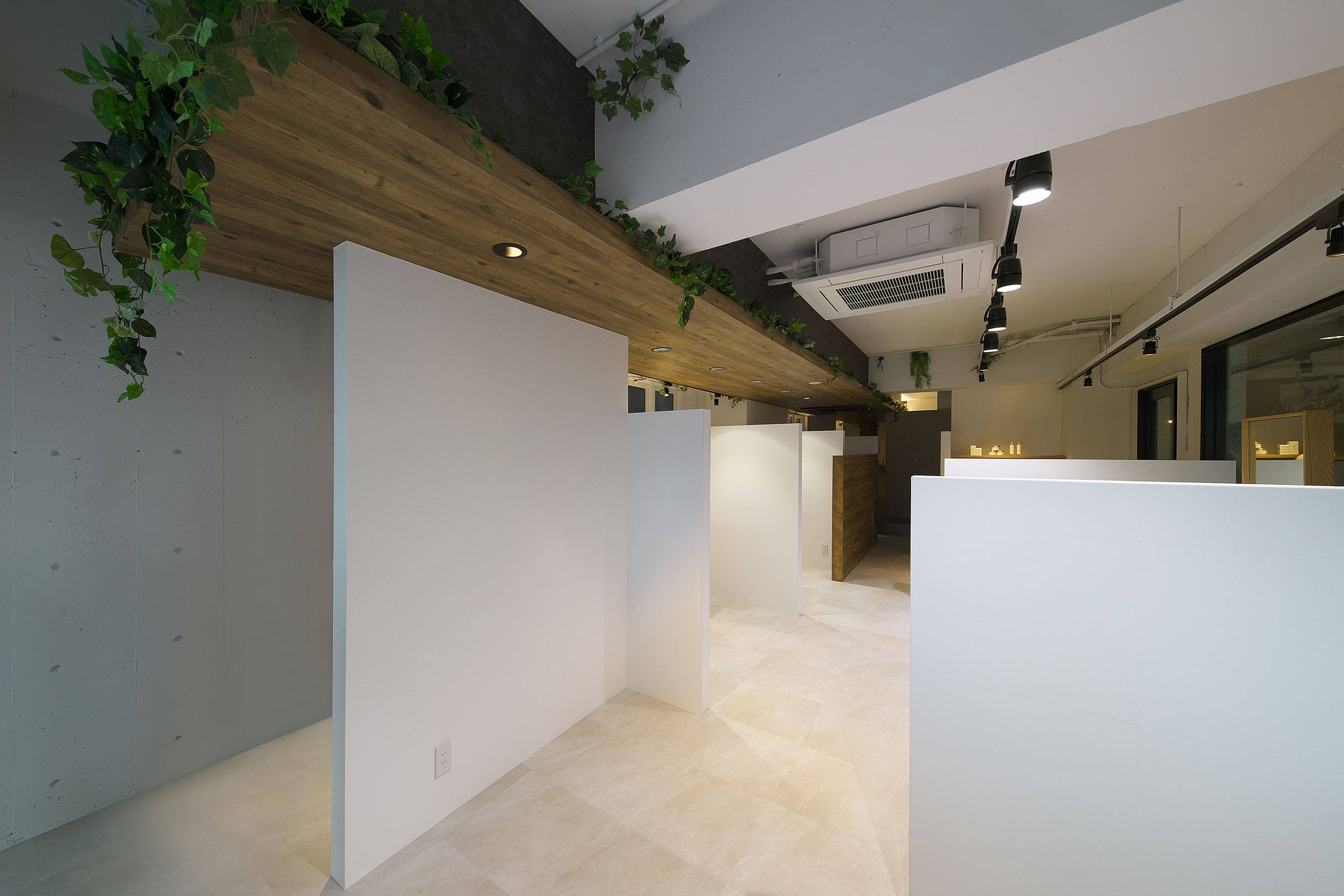 塚口の美容室 bloom hair design 本店の店内。白い仕切りの半個室が並び、木の梁にグリーンが下がる